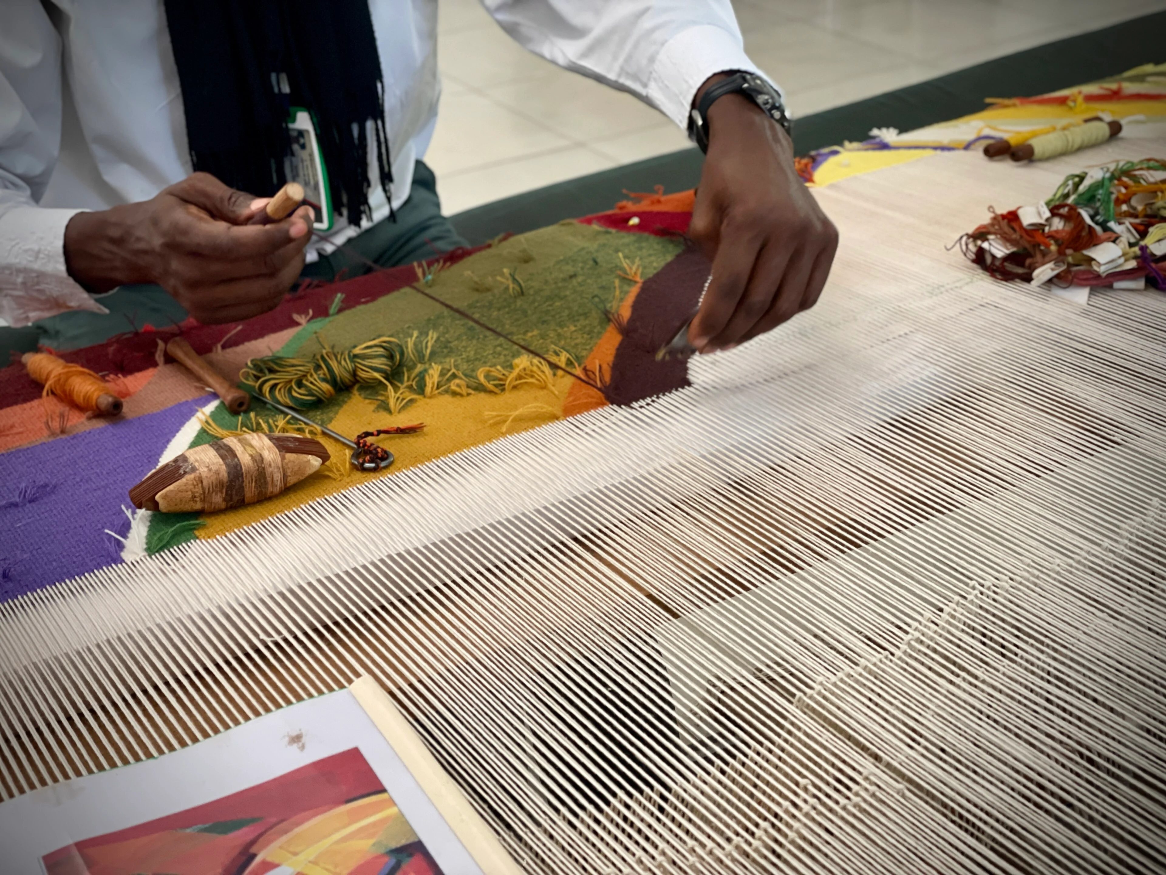 A Senegalese craftsperson works close to the surface of a handwoven carpet.