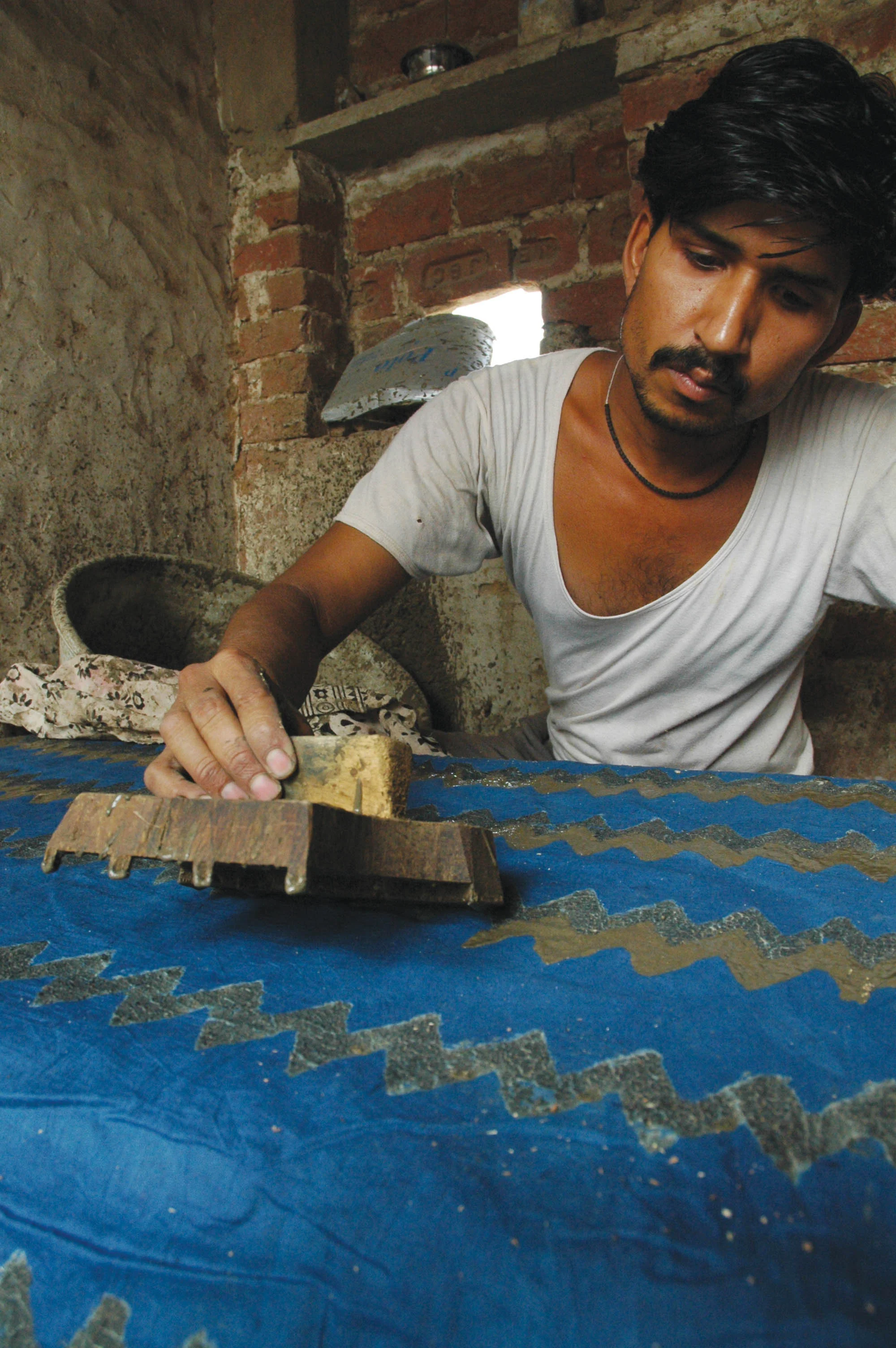 A printer presses a carved wooden block onto prepared fabric by hand.